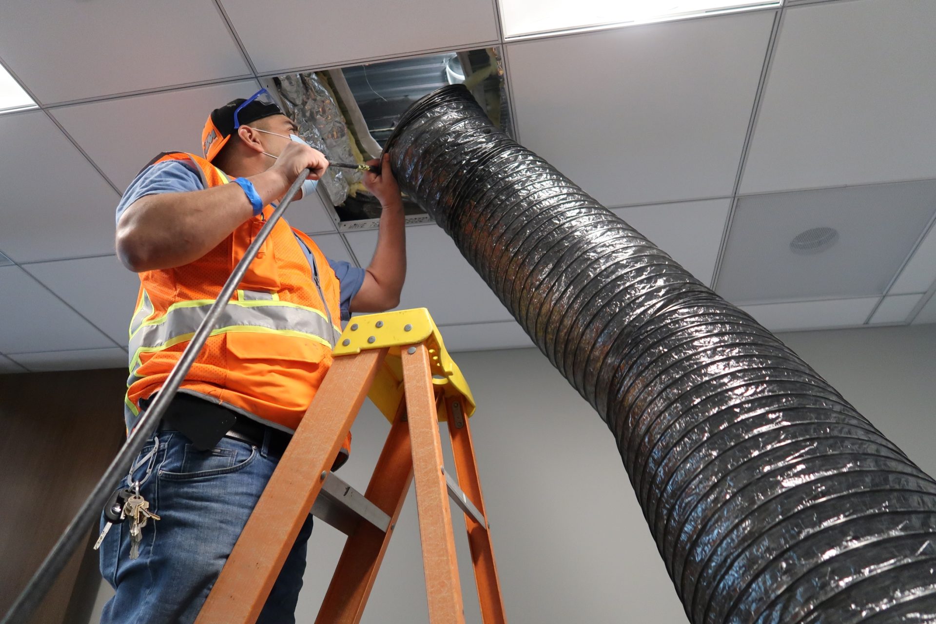 Technician cleaning commercial ceiling ductwork with a large extraction hose